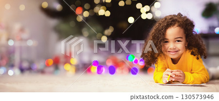 Christmas fun. Adorable little afro girl lying on floor near Xmas tree, empty space 130573946
