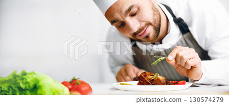 Professional Chef Man In Uniform Decorating Dish Cooking Chicken In Restaurant Kitchen Indoor. Food Presentation Concept. Selective Focus Professional Chef Man In Uniform Decorating Dish Cooking Chicken In Restaurant Kitchen Indoor. Food Presentation Concept. Selective Focus 130574279