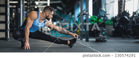 A man performs a side stretch on the gym floor, focusing on flexibility and strength during his training routine, copy space A man performs a side stretch on the gym floor, focusing on flexibility and strength during his training routine, copy space 130574291