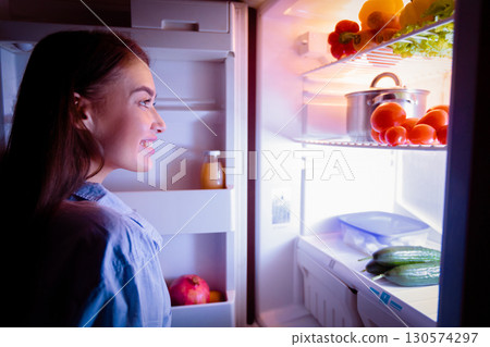 Millennial woman raiding refrigerator late at night, looking for healthy snack, free space 130574297
