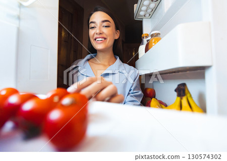 Preparing healthy lunch. Young woman taking fresh tomato from refrigerator, view from inside, empty space 130574302