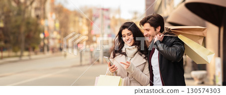 Order taxi online. Couple using smartphone after shopping in modern boutiques outdoors, copy space Order taxi online. Couple using smartphone after shopping in modern boutiques outdoors, copy space 130574303