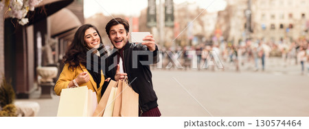 Couple recording video for fashion blog after shopping in mall, walking outdoors, panorama with copy space Couple recording video for fashion blog after shopping in mall, walking outdoors, panorama with copy space 130574464