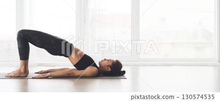 A person stretching on a mat, practicing meditation with a tranquil expression in a well-lit yoga studio, copy space A person stretching on a mat, practicing meditation with a tranquil expression in a well-lit yoga studio, copy space 130574535