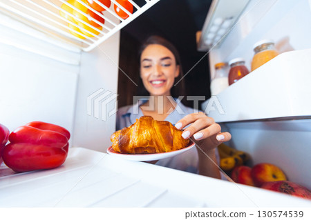 Tasty dessert. Cheerful girl taking yummy croissant from refrigerator at home, view from inside Tasty dessert. Cheerful girl taking yummy croissant from refrigerator at home, view from inside 130574539