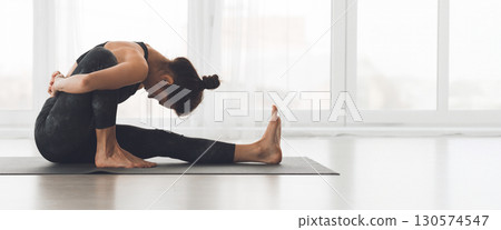 A woman performs a seated yoga pose in a spacious, sunlit studio, focusing on her breath and balance, copy space A woman performs a seated yoga pose in a spacious, sunlit studio, focusing on her breath and balance, copy space 130574547