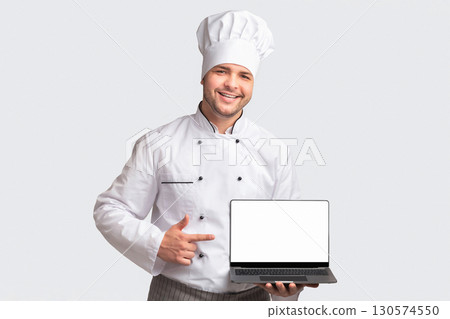 Chef Man Holding Laptop With Blank Screen Pointing Finger Standing Over White Studio Background. Cooking And Recipes Website. Panorama 130574550