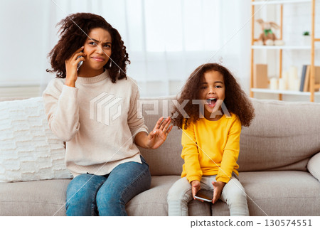 Loud Child. Little Daughter Shouting While Afro Mother Talking On Phone Sitting On Couch At Home 130574551