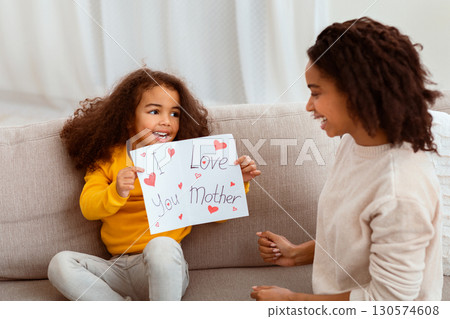 Happy Mother's Day Concept. Daughter Congratulating Mother Giving Postcard Celebrating Holiday Together Sitting On Couch Indoor 130574608