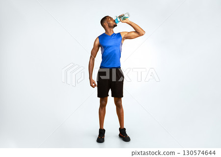 Stay Hydrated. Full length muscular afro man drinking water from bottle over yellow studio background, copyspace Stay Hydrated. Full length muscular afro man drinking water from bottle over yellow studio background, copyspace 130574644
