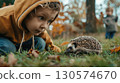 Curious child watches hedgehog resting in grass, great for nature study and discovery 130574670
