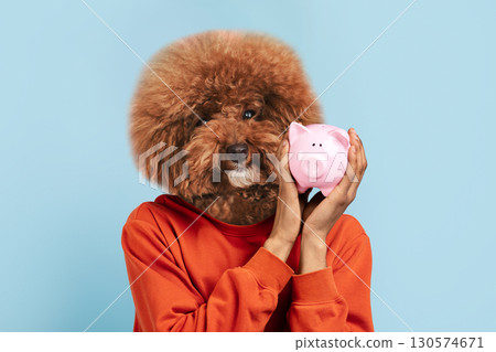 A playful moment captures an individual with a fluffy dog head, holding a pink piggy bank closely. The backdrop features a light blue hue, enhancing the whimsical atmosphere. A playful moment captures an individual with a fluffy dog head, holding a pink piggy bank closely. The backdrop features a light blue hue, enhancing the whimsical atmosphere. 130574671