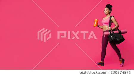 On a way to gym. Beautiful afro woman with yoga mat, sporty bag and shaker in hand going towards copy space 130574875