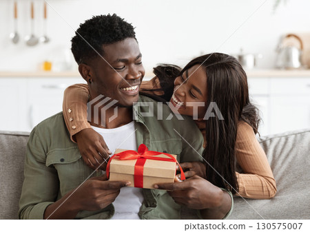 Emotional african american woman hugging lover, giving gift box, making great surprise for St. Valentines Day, home interior, free space. Happy black lady embracing her husband, holding present 130575007