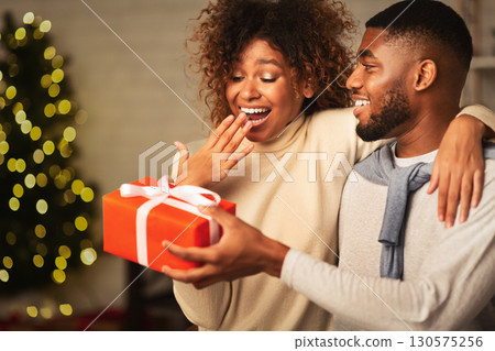 African-american couple celebrating Christmas at home, man giving surprise to wife, free space African-american couple celebrating Christmas at home, man giving surprise to wife, free space 130575256