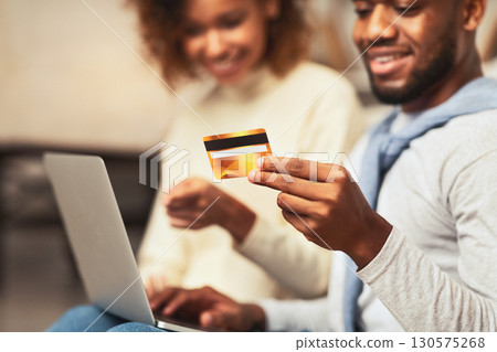 Internet shopping. Black couple ordering clothes with credit card, using laptop, closeup Internet shopping. Black couple ordering clothes with credit card, using laptop, closeup 130575268