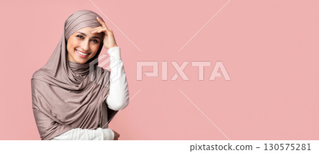 Shy arab women in hijab smiling and touching head in embarrassing, posing over pink background with free space Shy arab women in hijab smiling and touching head in embarrassing, posing over pink background with free space 130575281