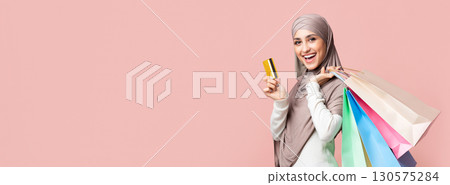 Happy customer. Joyful muslim girl in hijab with colorful shopping bags and credit card over pink studio background and looking at camera, empty space Happy customer. Joyful muslim girl in hijab with colorful shopping bags and credit card over pink studio background and looking at camera, empty space 130575284