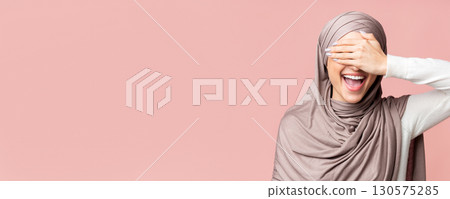 Happy Muslim Girl In Hijab Covering Eyes With Hand And Smiling, Having Fun Over Pink Background, Free Space 130575285