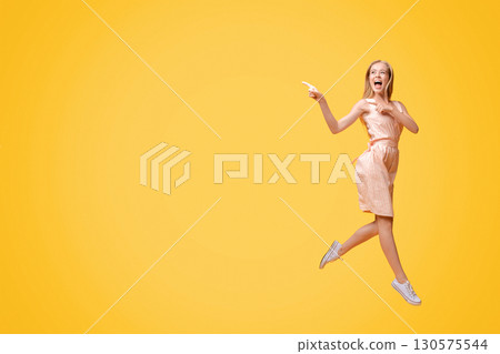 Great Offer. Excited Teen Girl In Summer Dress Jumping In Air And Pointing Aside At Copy Space On Yellow Background Great Offer. Excited Teen Girl In Summer Dress Jumping In Air And Pointing Aside At Copy Space On Yellow Background 130575544