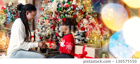 Merry Christmas. African american mother and daughter exchanging gifts sitting under Xmas tree at home, side view Merry Christmas. African american mother and daughter exchanging gifts sitting under Xmas tree at home, side view 130575550