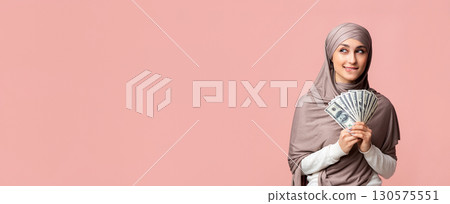 Ready for shopping. Pensive arabic woman in hijab holding dollar cash and thinking how to spend money, posing over oink background with free space Ready for shopping. Pensive arabic woman in hijab holding dollar cash and thinking how to spend money, posing over oink background with free space 130575551