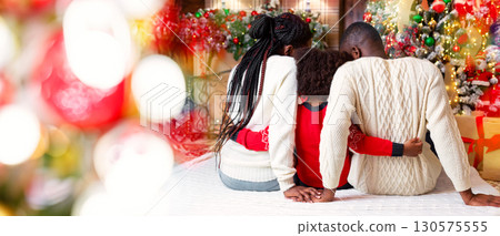 Family Christmas. Rear view of black couple and their daughter celebrating winter holidays together, little girl hugging parents Family Christmas. Rear view of black couple and their daughter celebrating winter holidays together, little girl hugging parents 130575555
