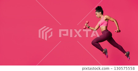 Active young black woman training wth dumbbells over red background, side view 130575558