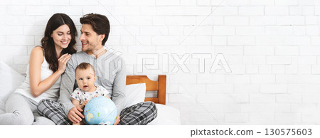 A joyful family sits on a comfortable couch, sharing special moments together. The parents lovingly engage with their baby, showcasing a globe, suggesting a sense of adventure and exploration A joyful family sits on a comfortable couch, sharing special moments together. The parents lovingly engage with their baby, showcasing a globe, suggesting a sense of adventure and exploration 130575603