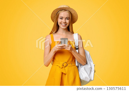 Online Map App Concept. Young Girl Tourist Holding Smartphone In Hands, Wearing Hat And Backpack, Posing Over Yellow Studio Background Online Map App Concept. Young Girl Tourist Holding Smartphone In Hands, Wearing Hat And Backpack, Posing Over Yellow Studio Background 130575611