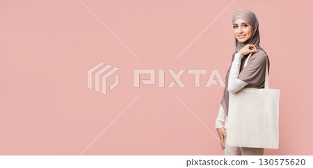 Eco Bag. Smiling Muslim Girl In Hijab With Blank Canvas Tote Handbag Over Pink Studio Background, Free Space Eco Bag. Smiling Muslim Girl In Hijab With Blank Canvas Tote Handbag Over Pink Studio Background, Free Space 130575620