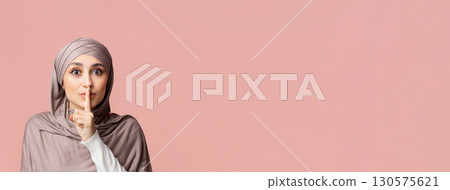 Secret Concept. Young arabic woman in hijab showing hush sign, putting finger on lips, gesturing keep silence over pink studio background, empty space 130575621