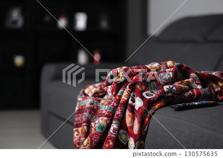 Cozy living room featuring a colorful blanket draped on a black sofa with remote control nearby 130575635