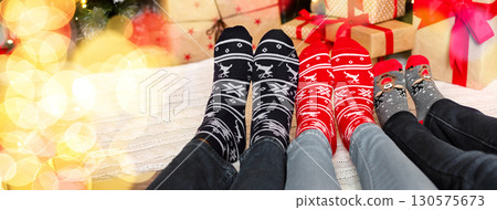 Christmas atmosphere background. Three pairs of feet in warm socks with winter holiday print ornament, panorama 130575673