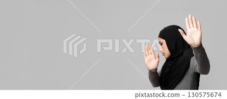 Stop Violence. Scared muslim woman in hijab showing stop sign with open palms, protecting herself from abuse over gray background with free space 130575674