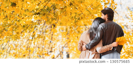 Back view of couple hugging and walking together by autumn forest, panorama with empty space 130575685