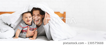 A father and his baby share a moment of laughter while playing under a cozy blanket. The warm atmosphere highlights their bond, showcasing the happiness and love between them, copy space A father and his baby share a moment of laughter while playing under a cozy blanket. The warm atmosphere highlights their bond, showcasing the happiness and love between them, copy space 130575688