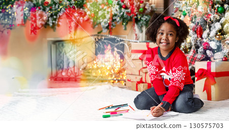 Portrait of adorable afro girl sitting on floor writing letter to Santa 130575703