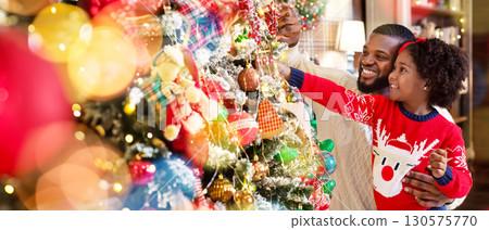 Cute little african girl decorating Christmas tree with her dad, enjoying winter holidays at home 130575770