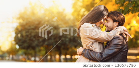 Loving young couple cuddling over golden forest background, touching each other with foreheads Loving young couple cuddling over golden forest background, touching each other with foreheads 130575780