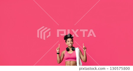 New ladies gym opening. Happy african american sporty girl with towel and earphones pointing up over red background New ladies gym opening. Happy african american sporty girl with towel and earphones pointing up over red background 130575800