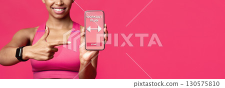 Cropped of smiling afro fitness lady pointing at workout application on mobile phone screen, red background, free space 130575810