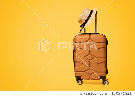 Travel Concept. Hand luggage suitcase with hat on it over yellow studio background with copy space 130575821