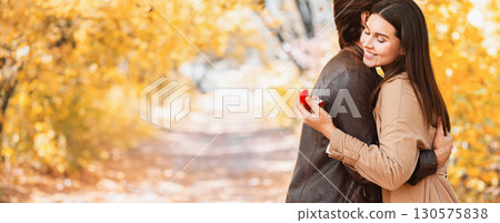 Marriage proposal at autumn forest. Happy woman looking at proposal ring while hugging her boyfriend, copy space 130575838