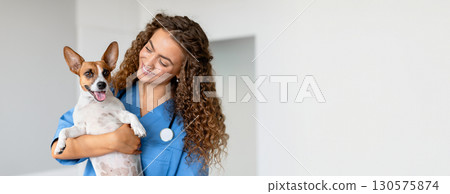 Woman vet in blue uniform smiling as she holds small white and brown dog, providing professional care in a well-lit animal health clinic, copy space Woman vet in blue uniform smiling as she holds small white and brown dog, providing professional care in a well-lit animal health clinic, copy space 130575874