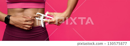 Close up of afro woman in sportswear measuring her body fat with fat caliper, red background 130575877