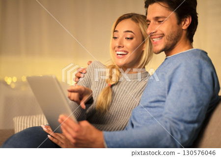 Happy couple searching gifts for christmas and using digital tablet, spending cold evening at home 130576046