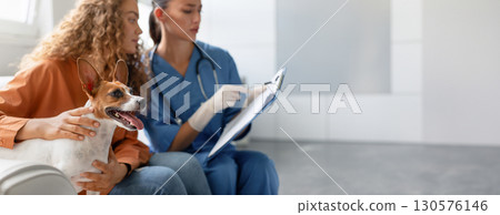 Attentive vet takes clinical notes while a pet owner lovingly strokes her happy Jack Russell Terrier at a routine vet appointment in a bright clinic, copy space Attentive vet takes clinical notes while a pet owner lovingly strokes her happy Jack Russell Terrier at a routine vet appointment in a bright clinic, copy space 130576146