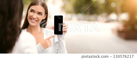 App recommended share information concept. Cheerful woman showing her friend blank smartphone screen, empty space for mockup 130576217
