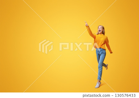 Big sales. Excited beautiful teen jumping and pointing finger aside, orange background with copy space Big sales. Excited beautiful teen jumping and pointing finger aside, orange background with copy space 130576433